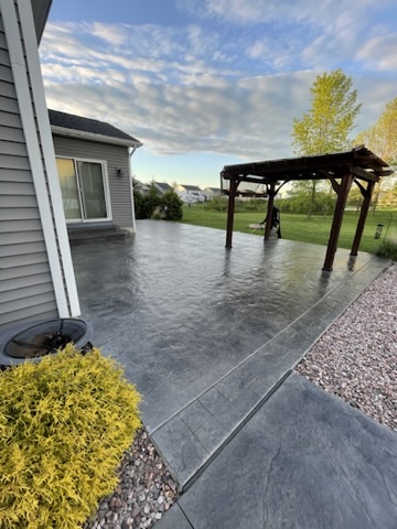 843BC461-2D67-42D5-B2A4-16E81BA98B6D_4_5005_c Concrete patio with pergola, glass door, yellow shrub, and gravel area Cody X Pressure Washing