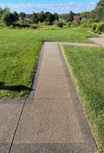 Photo Aug 10 2022, 5 28 08 PM A concrete path on a green lawn, sunny with trees and homes behind. Cody-X Pressure Washing