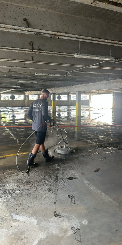 Photo Aug 16 2024, 11 26 13 AM Cody-X worker in boots pressure washes a parking garage floor, leaving wet sections. Cody-X Pressure Washing