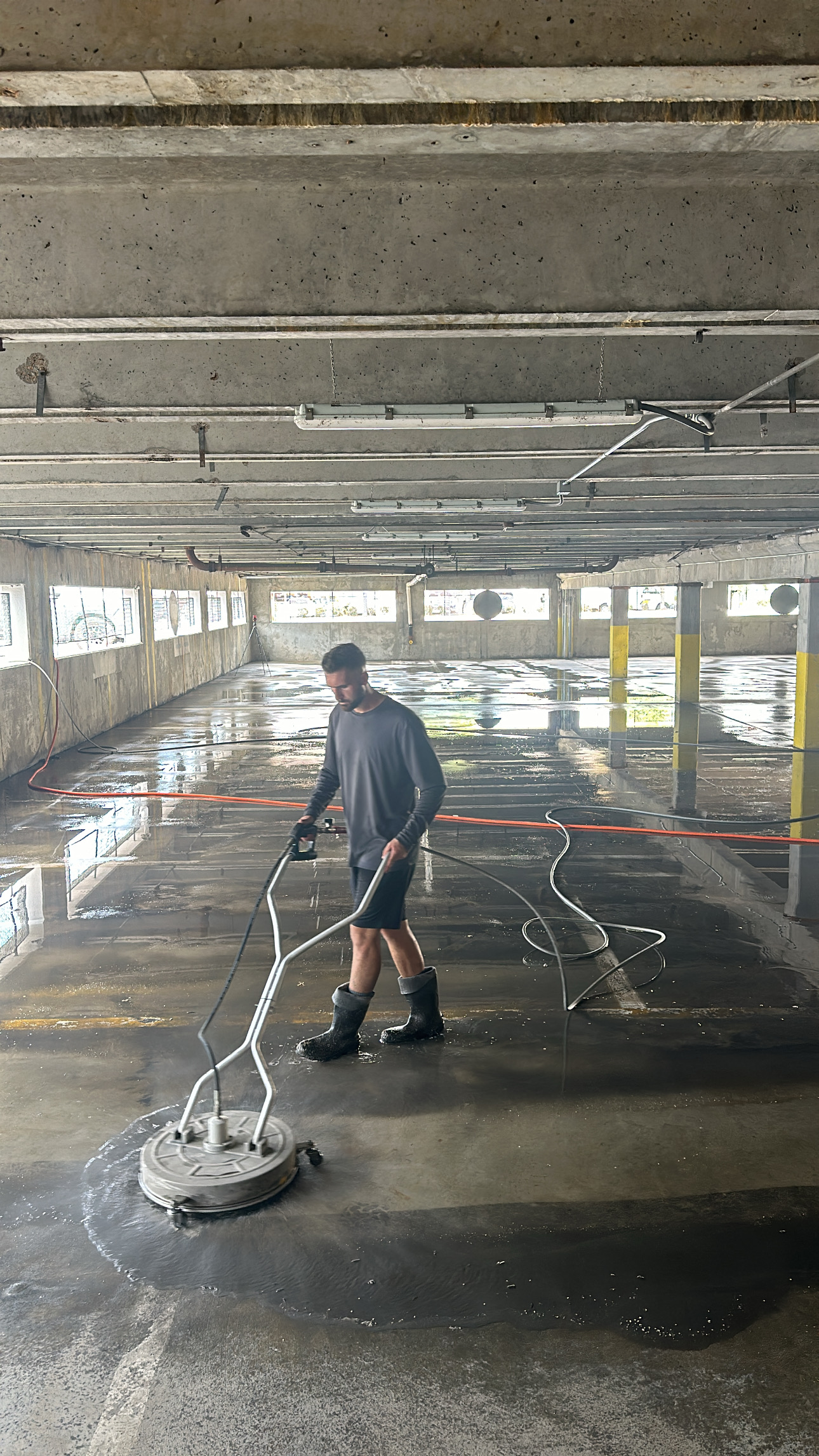 Photo Aug 16 2024, 11 27 20 AM Boot wearing worker uses a floor cleaner on parking garage concrete Cody X Pressure Washing