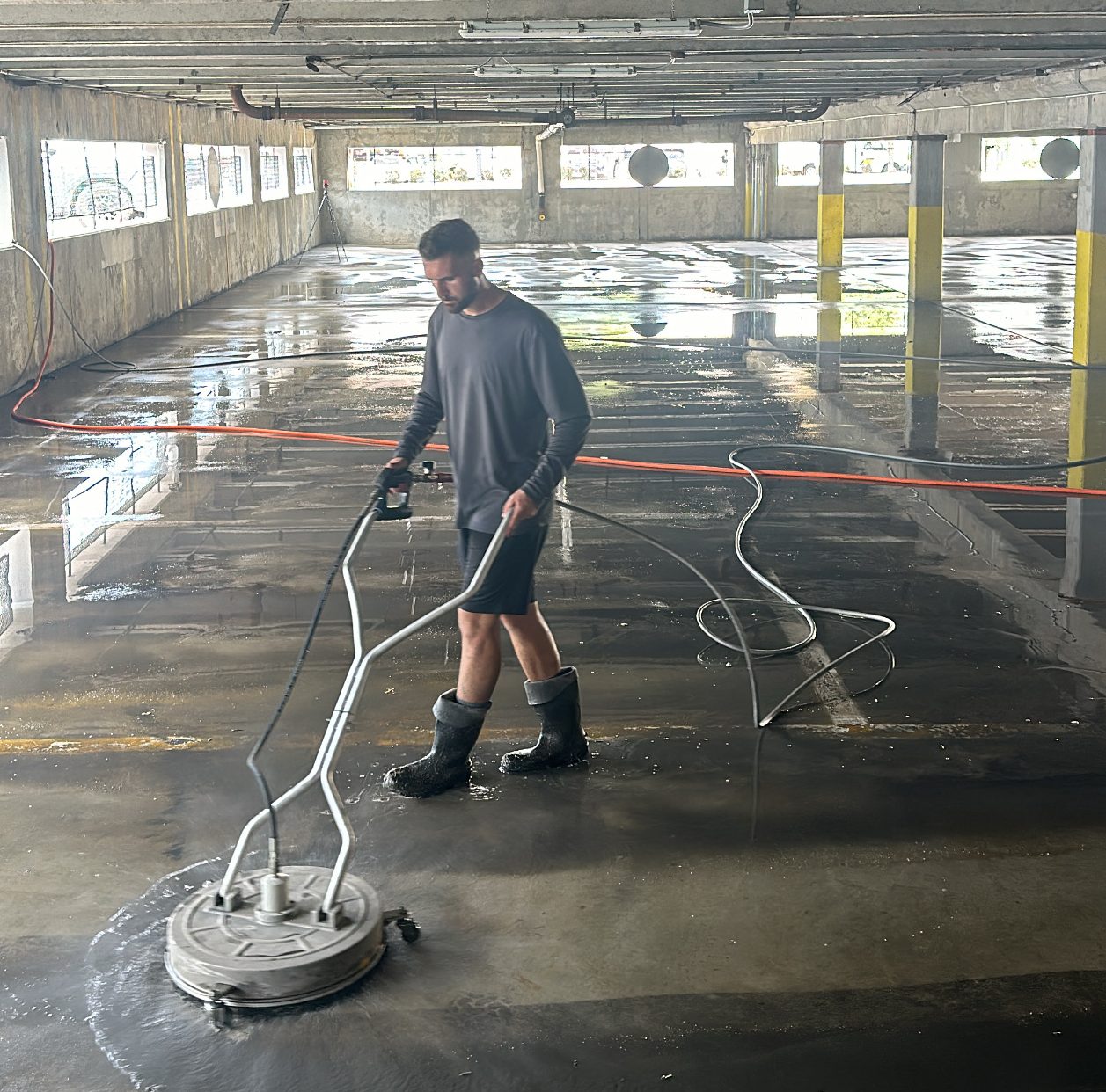 Photo Aug 16 2024, 11 27 20 AM Person in boots uses a floor cleaning machine in a wet parking garage Cody X Pressure Washing