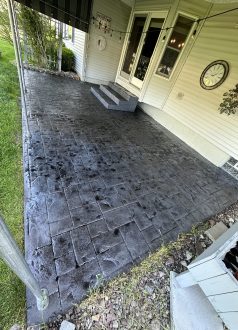 Photo May 27 2023, 9 03 00 AM Stamped concrete patio with steps, plants, and wall clock by house. Cody-X Pressure Washing