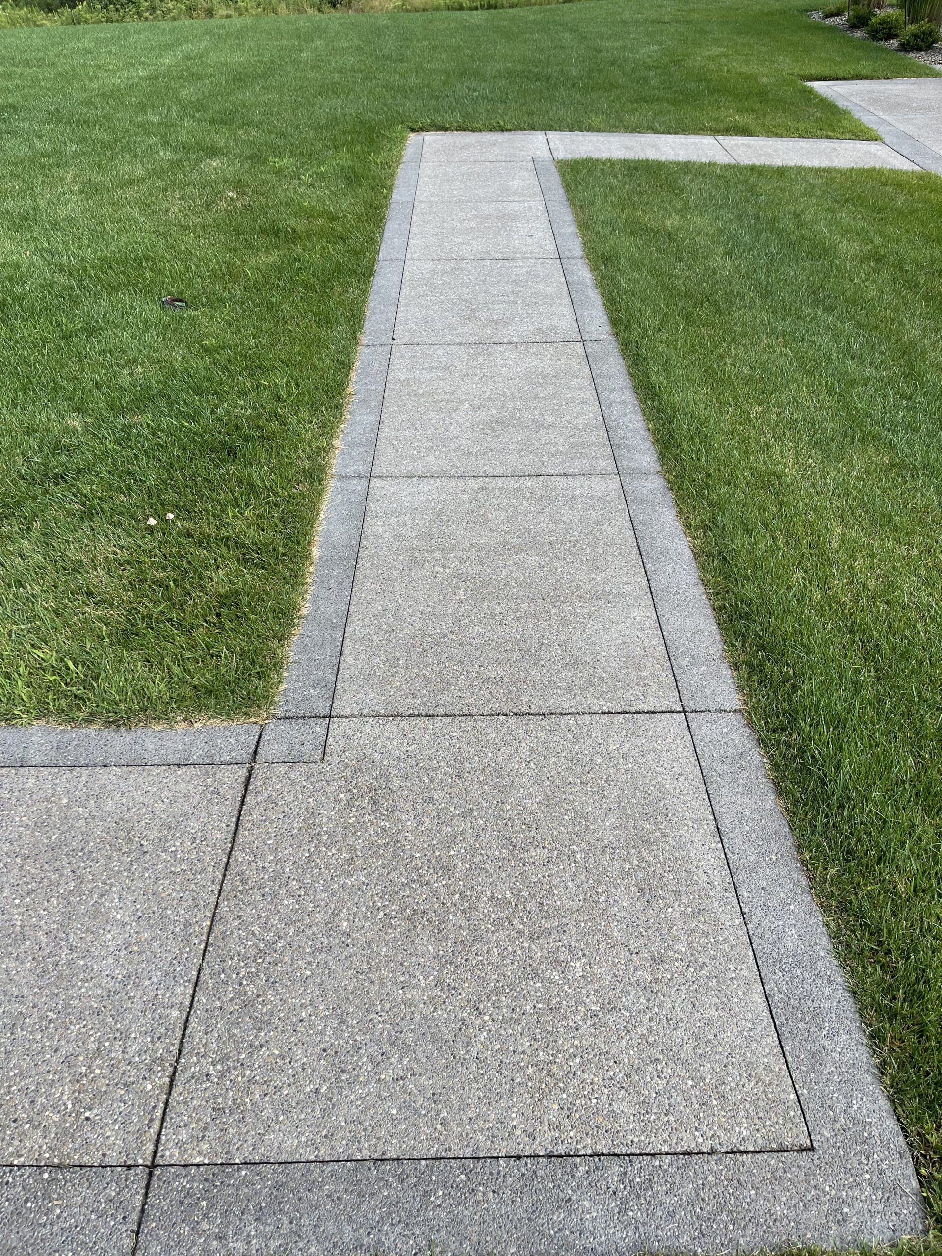 Photo Aug 10 2022, 10 09 05 AM Concrete sidewalk with sharp turns, bordered by vibrant green grass Cody X Pressure Washing