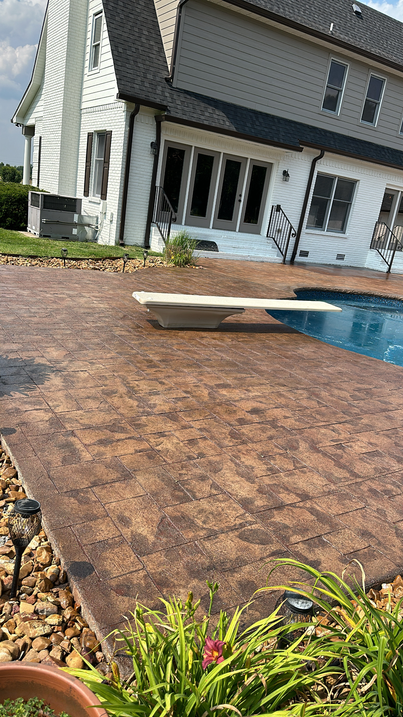 0D01FEF7-BE01-4885-9D97-1F8300EC53B4 Backyard pool, tiled patio, diving board, rocks, two story house behind Cody X Pressure Washing