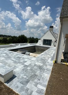 82B7DC44-1EE4-45CB-B02E-AD42806D9EE0 Partially built pool with stone tiles beside a white house under clouds. Cody-X Pressure Washing