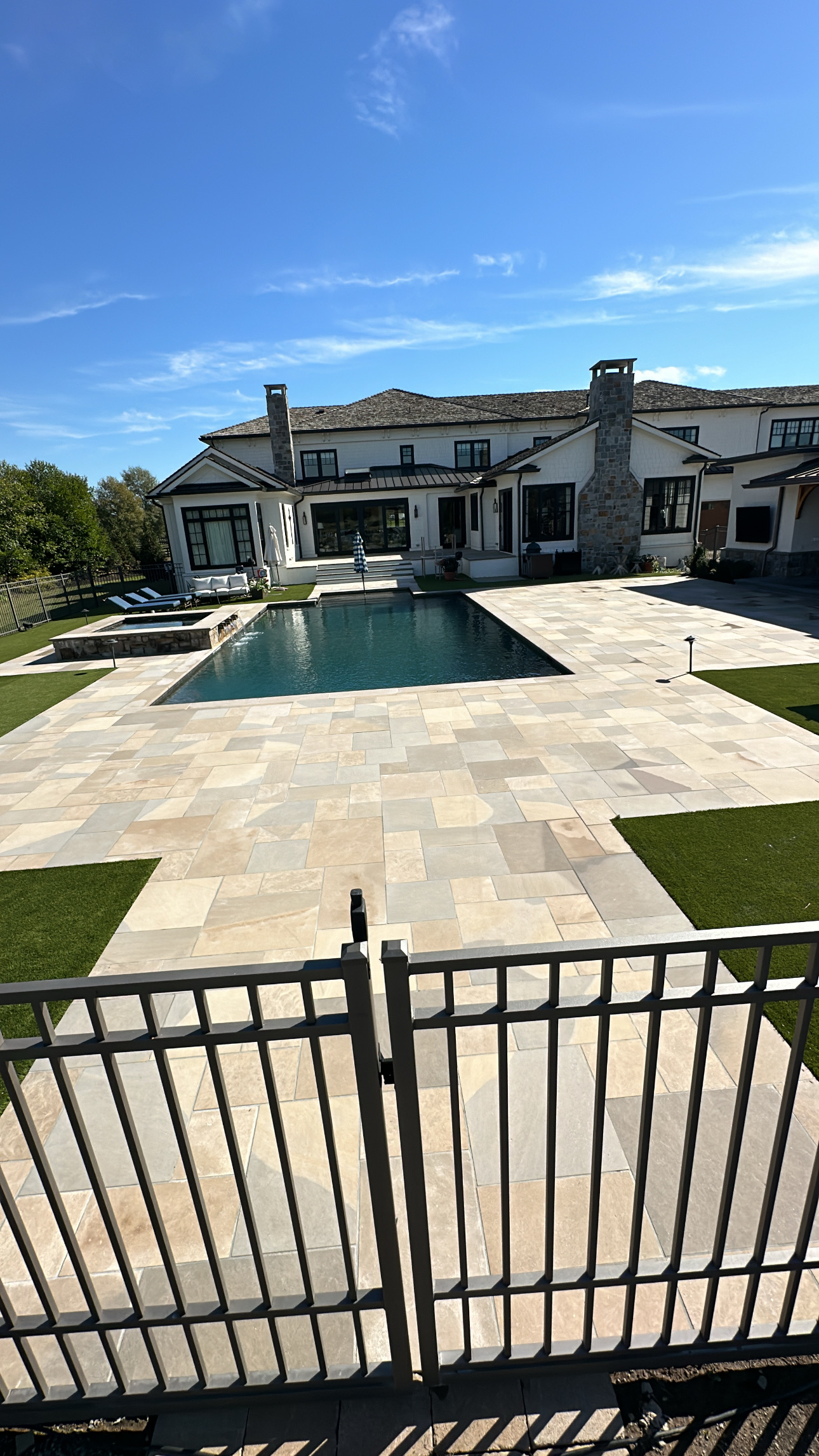 CBAA8EBC-BC00-4576-BA5B-B87BDB01B104 Modern house with stone chimney, pool, patio, and metal fence in sunlight Cody X Pressure Washing