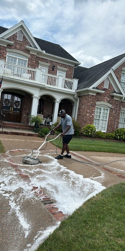 DBB4B7E3-50C4-4DF5-BA3F-45C676952109 Person pressure washes soapy driveway at brick house for Cody-X service. Cody-X Pressure Washing