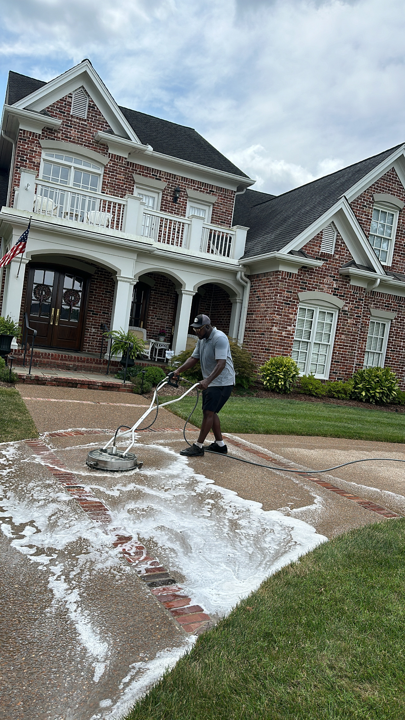 DBB4B7E3-50C4-4DF5-BA3F-45C676952109 Person pressure washes soapy driveway at brick house for Cody X service Cody X Pressure Washing