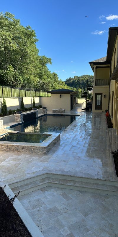 Modern backyard with pool, hot tub, stone patio, and lush trees. Cody-X Pressure Washing