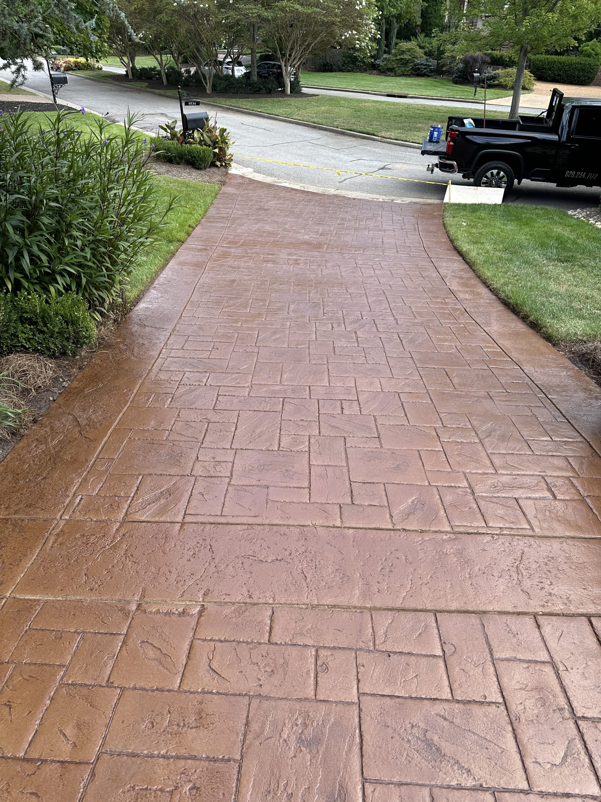 IMG_0409 Wet patterned concrete driveway slopes to a street with lawns and a black truck Cody X Pressure Washing