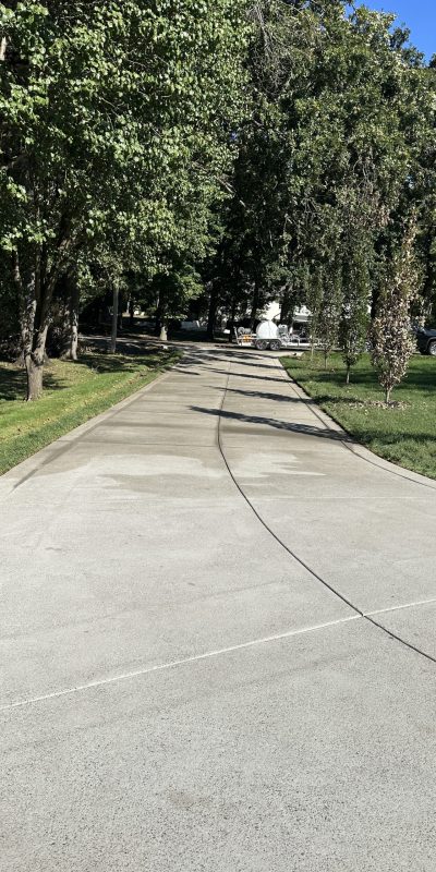 IMG_0669 Concrete driveway with green grass, shade trees, and parked vehicles. Cody-X Pressure Washing