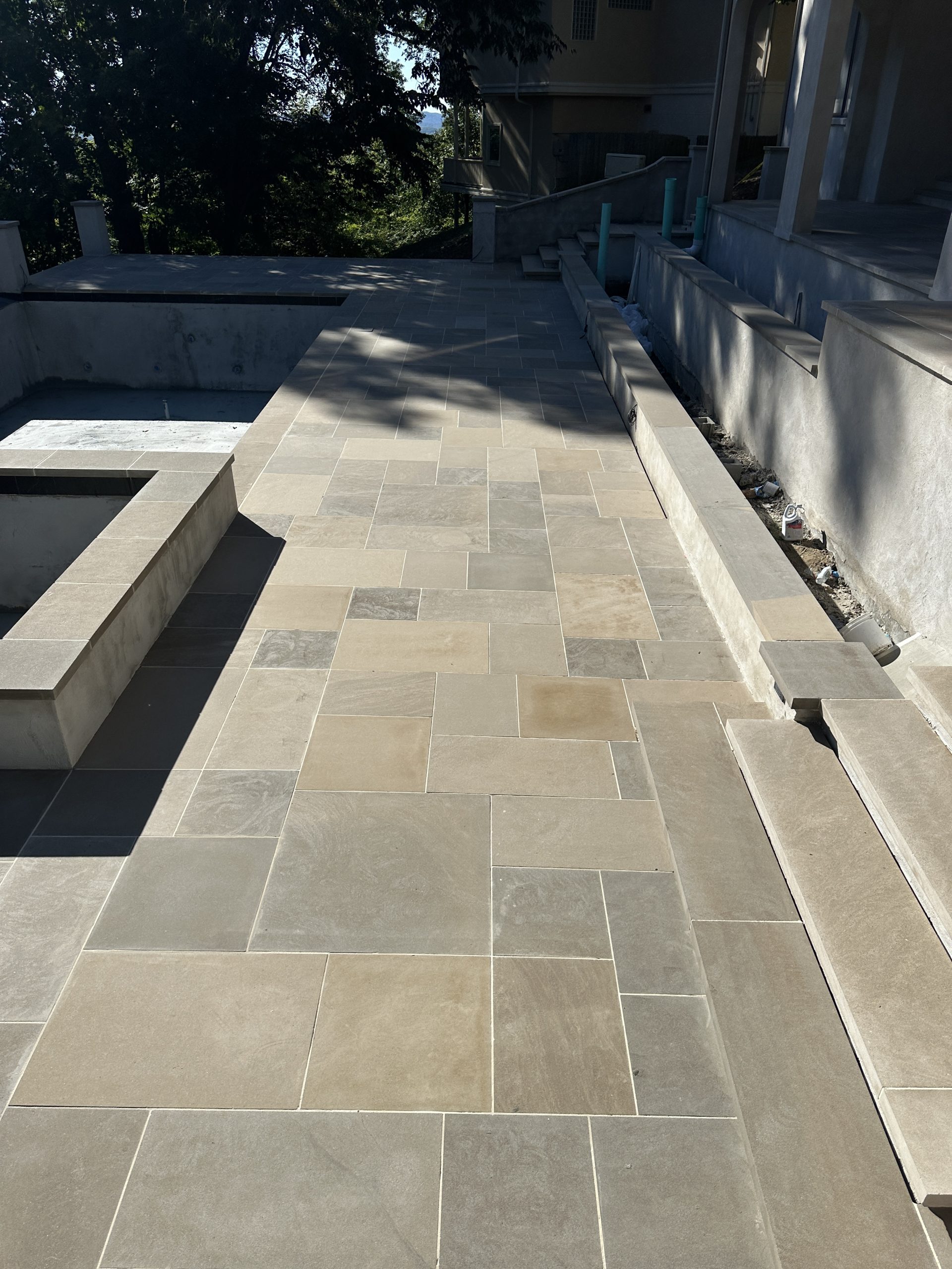 IMG_0723 Outdoor walkway with beige and gray stone tiles, bordered by concrete steps Cody X Pressure Washing