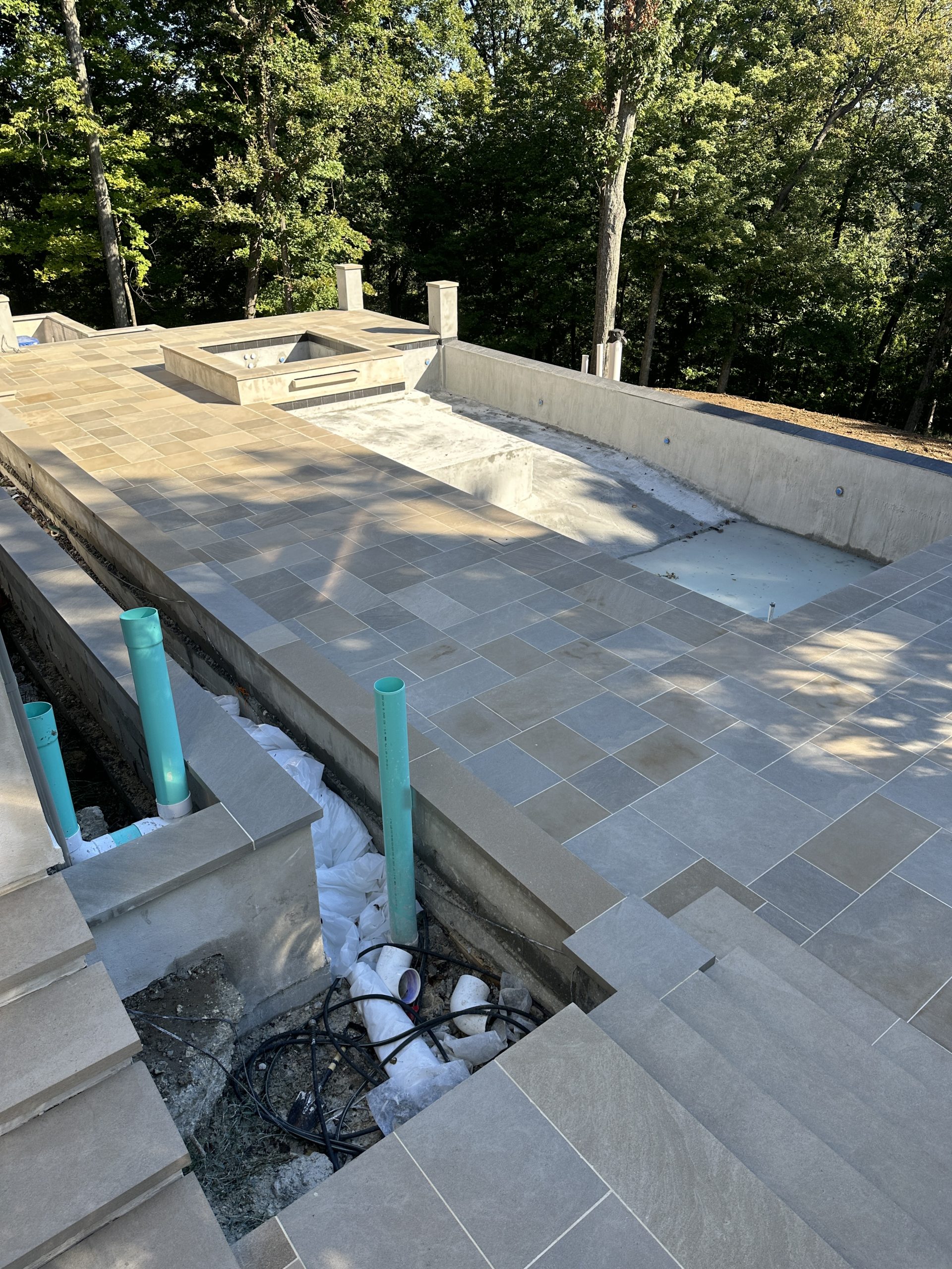 IMG_0728 Unfinished pool area with tiled deck, exposed pipes, and trees Cody X Pressure Washing