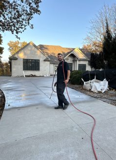 IMG_1187 A man with a red hose stands on a new driveway, tools and materials nearby. Cody-X pressure washing and sealing service. Cody-X Pressure Washing