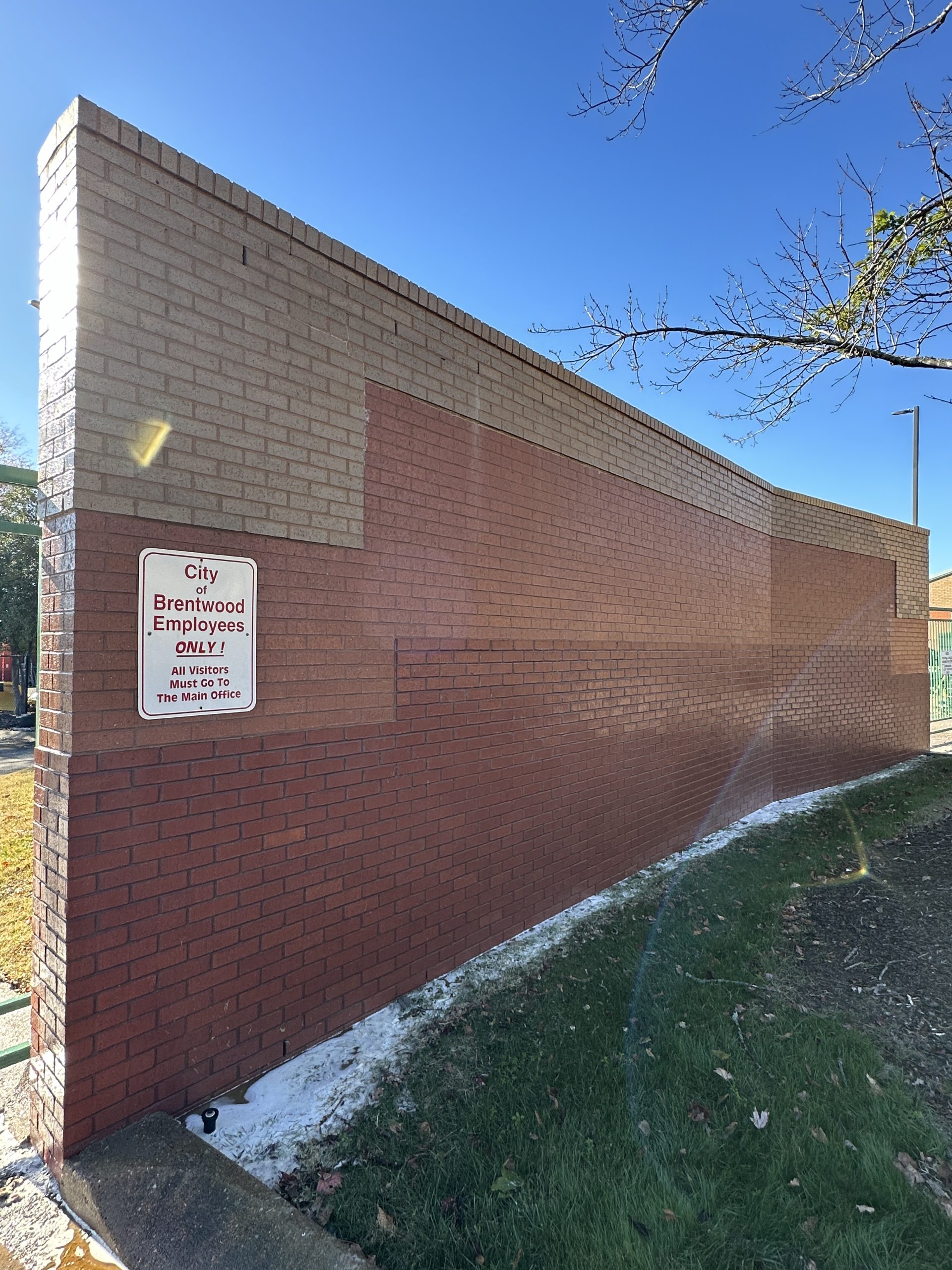 IMG_1296 A brick wall with patchy paint and a Brentwood employee sign under blue sky Cody X Pressure Washing