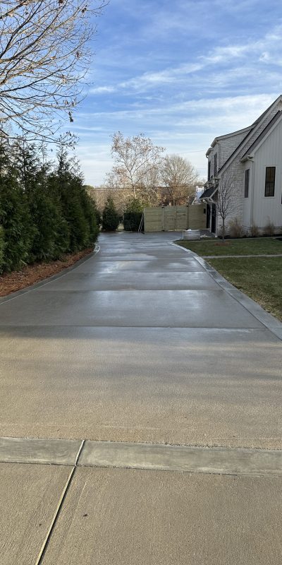 Clean driveway leads to white house, green lawn, and trees under clouds. Cody-X Pressure Washing