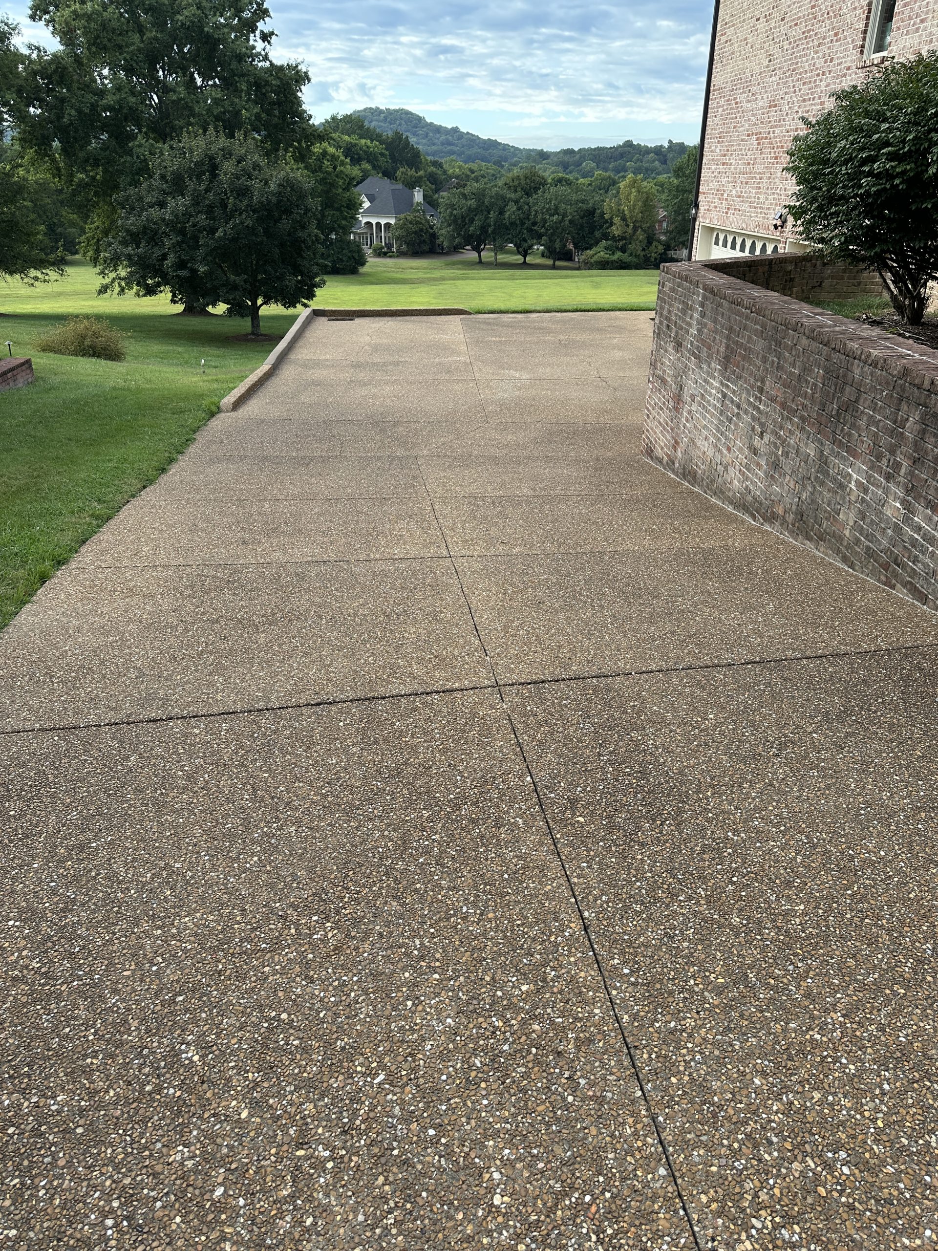 IMG_9866 Concrete driveway by brick house, bordered by grass and trees under clouds Cody X Pressure Washing