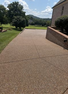 IMG_9968 Concrete driveway by brick house, bordered by grass, trees in background. Cody-X Pressure Washing