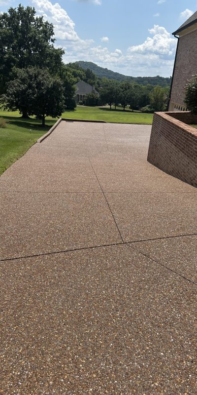 IMG_9968 Concrete driveway by brick house, bordered by grass, trees in background. Cody-X Pressure Washing