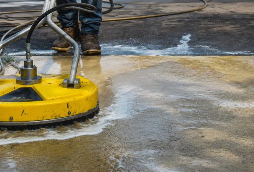 concrete wash hero Cody-X cleaning concrete sidewalk with yellow pressure washer; clean vs. dirty areas visible. Cody-X Pressure Washing