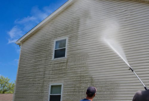 house wash hero Two people pressure wash a light house for Cody-X’s cleaning service. Cody-X Pressure Washing